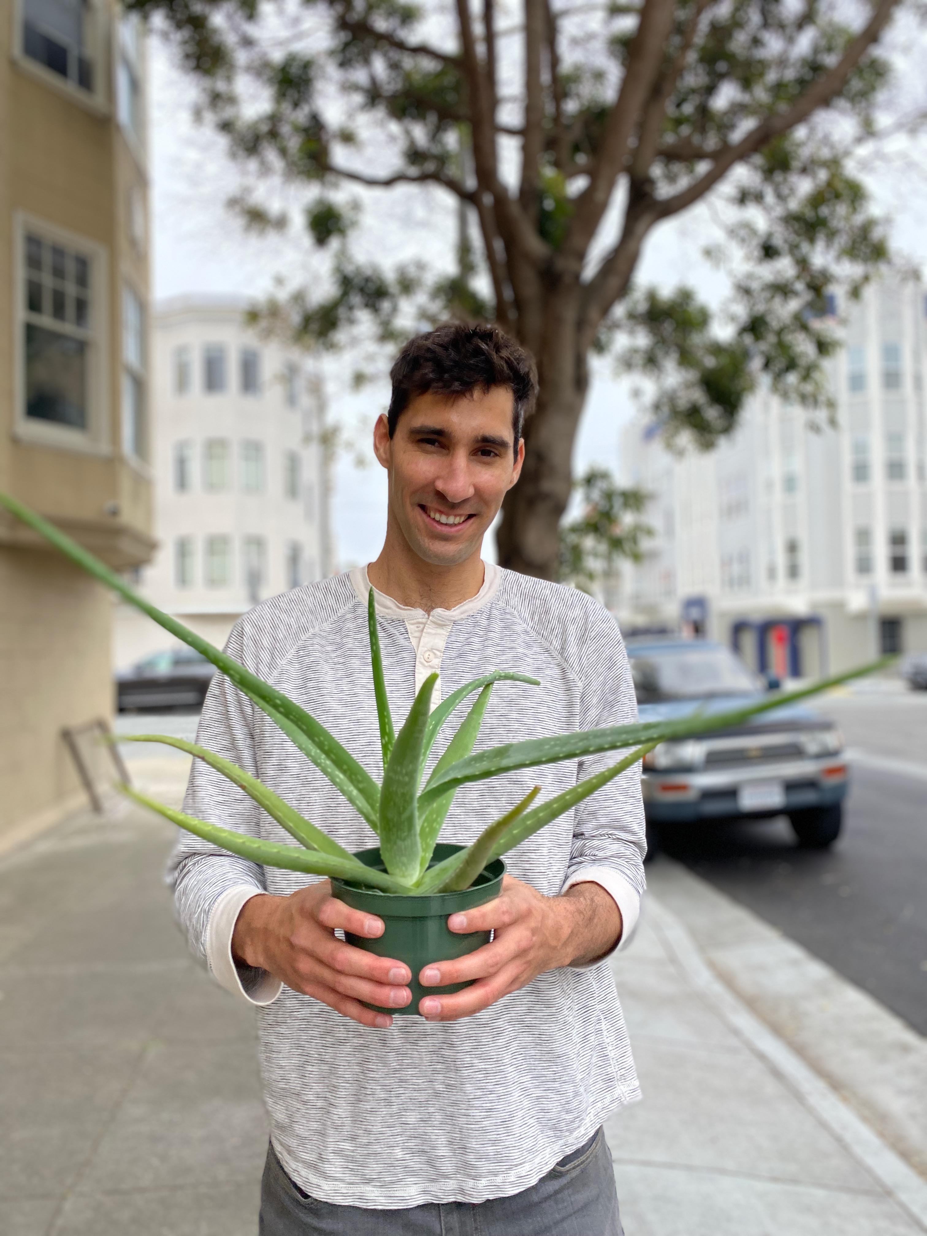 New plant parent smiling while holding a plant gifted by Reza Kaabi from Bank of Trees, ready to start their plant care journey.